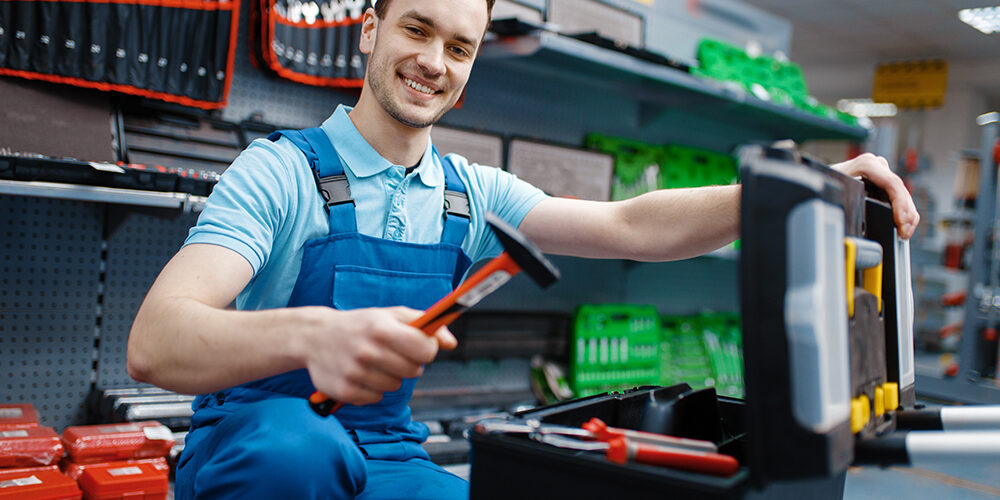 Happy male worker in uniform choosing toolbox in tool store. Choice of professional equipment in hardware shop, instrument supermarket