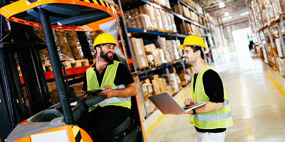 Warehouse workers working together with forklift loader trasnporter